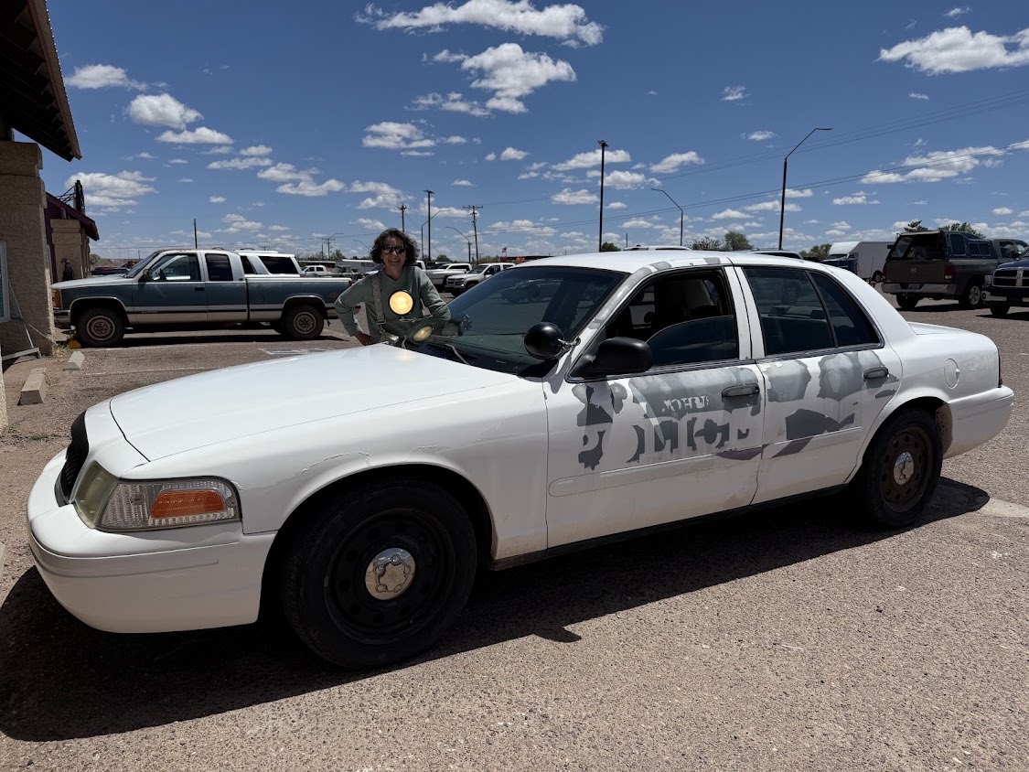 A retired white police cruiser with its decals half peeled off, used as an airport courtesy car